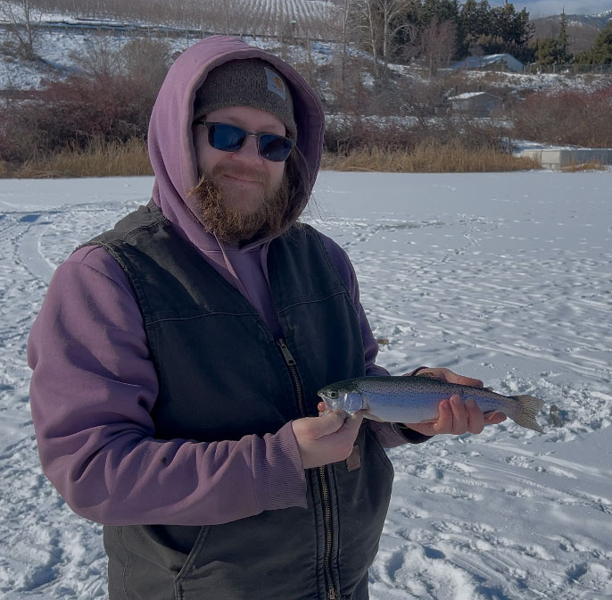 An angler at Roses Lake holding a freshly caught trout during a successful ice fishing trip