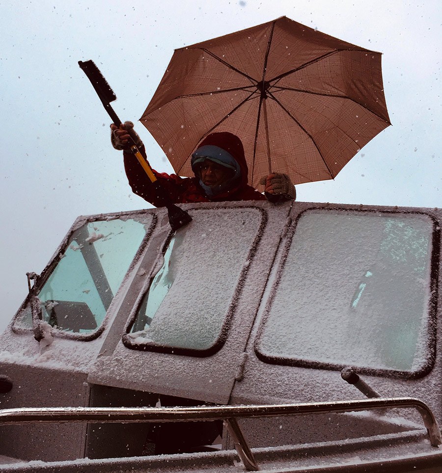 Eileen Graybill scraping snow and ice off the windshield of the boat on Lake Chelan